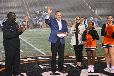 Dr. Marc Levine, John Mack, and Princeton cheerleaders on the Princeton football field, Dr. Levine is waving to the crowd